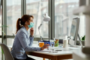 pensive businesswoman with face mask reading an e mail on deskto